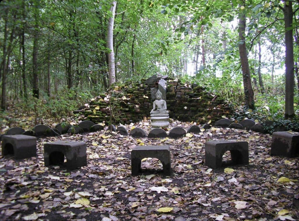 Boeddhabeeld op de Boeddhaplek in het bos, met stenen zitjes op de voorgrond