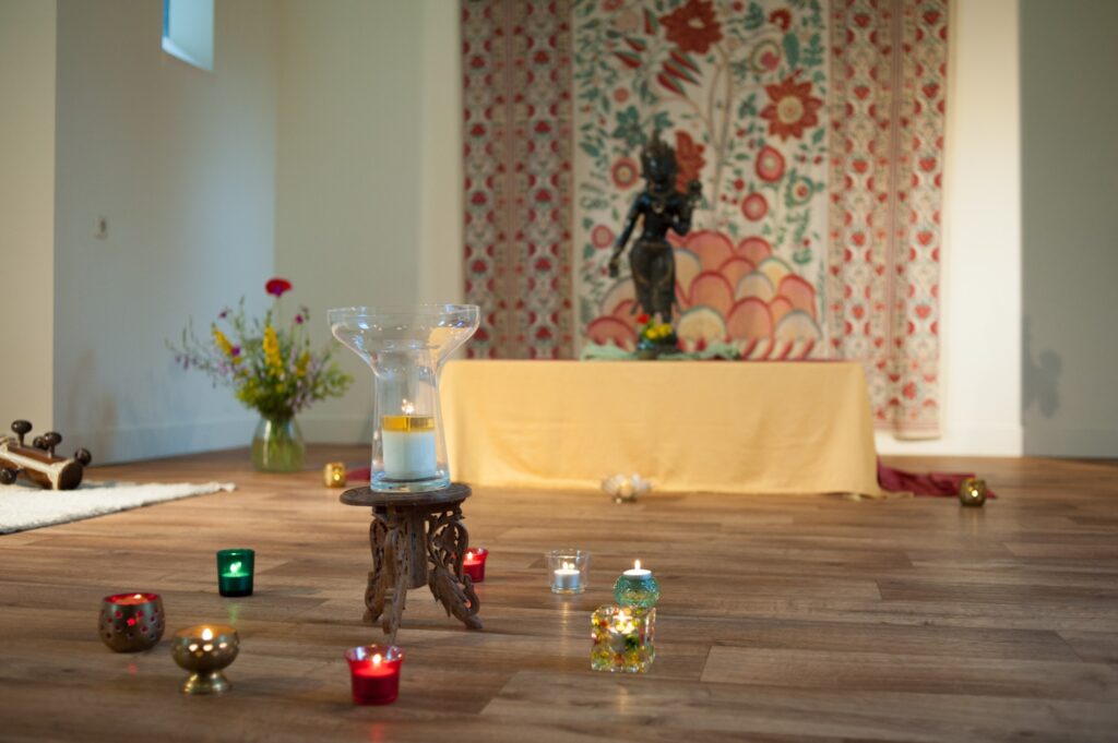 Ritueel in de kapel: glazen schaal met kaars en kleine kaarsjes op de vloer, vrouwelijk beeld op de achtergrond