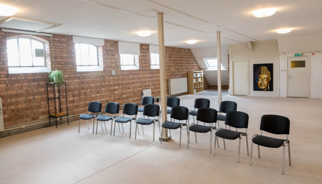 De Maanzaal op Landgoed de Leonardushoeve, met bakstenen wand, stoelen in een cirkelopstelling en een Boeddhabeeltenis achterin