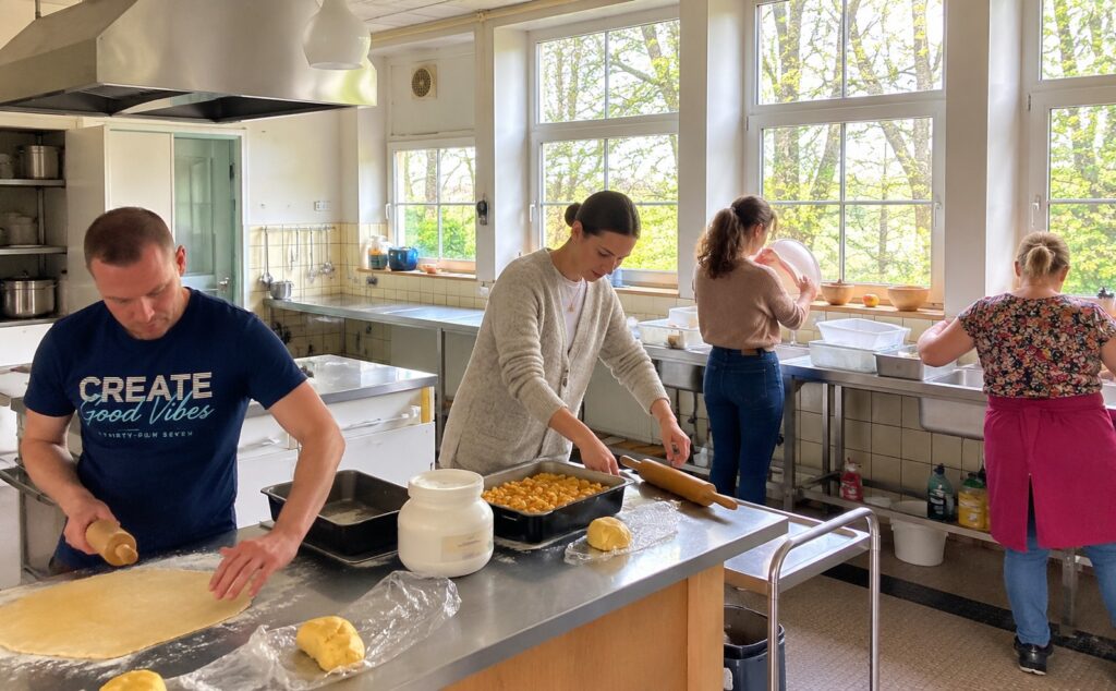 Vier mensen ieder met een eigen taak bezig in de keuken van Landgoed de Leonardushoeve: deeg uitrollen, koekjes vormen en afwassen